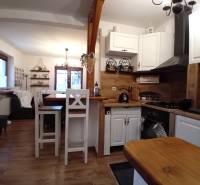 Rodinný dom, Vršatské Podhradie, okres Ilava - Kuchyňa a obývačka v rodinnom dome s podlahou s dreveným dekorom a bielym nábytkom.