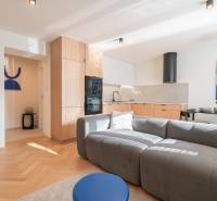 3i BYT V TOP LOKALITE – Trenčín, Sihoť - NA PRENÁJOM - Obývacia časť 3-izbového bytu s kuchyňou, sivou pohovkou a podlahou s dreveným dekorom.