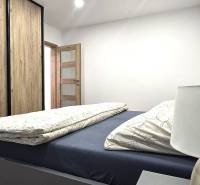 Prenájom komfortný, zariadený 3 izbový byt po úplnej rekonštrukcii - Spálňa s posteľou, skriňou s dreveným dekorom a lampou v 3-izbovom byte.