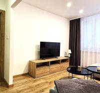 Prenájom komfortný, zariadený 3 izbový byt po úplnej rekonštrukcii - Obývačka v 3-izbovom byte s podlahou s dreveným dekorom a veľkým televízorom.