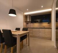 Exkluzívny 2i byt s terasou a parkovaním, Kramáre - Kuchyňa v 2-izbovom byte s dreveným dekorom, jedálenským stolom a čiernymi stoličkami.