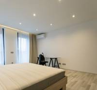 Exkluzívny 2i byt s terasou a parkovaním, Kramáre - Spálňa v 2-izbovom byte s posteľou, stolom a podlahou s dreveným dekorom.