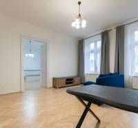 Priestranný 3i byt s vysokými stropmi, Dunajská - Obývacia izba v 3-izbovom byte s podlahou s dreveným dekorom a modrou sedačkou.