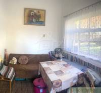 Rodinný dom v srdci Štiavnických vrchov, Štiavnické Bane. - Interiér rodinného domu s pohovkou, stolom, stoličkou a veľkým oknom s čipkovanými závesmi.