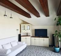 5-izb. dvojpodlažný rodinný dom, Rovinka - Obývačka v rodinnom dome so stropnými trámami, pohovkou, televíziou a veľkou rastlinou.