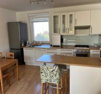 3-izb. byt, Palkovičova ul., Ružinov, lodžia, 4.p./12 - Kuchyňa v 3-izbovom byte s podlahou s dreveným dekorom, jedálenským stolom a barovým pultom.