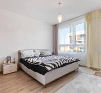 Novostavba 3-izb. bytu s parkovacím státím, ul.Hany Ponickej, Lamač - Svetlá spálňa v 3-izbovom byte s posteľou, nočným stolíkom a podlahou s dreveným dekorom.