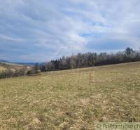 Stavebný pozemok s krásnym výhľadom nad obcou Jasenica pri Považskej B - Záhrady v Jasenici obklopené lúkami a lesným porastom pod zamračenou oblohou.