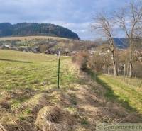 Stavebný pozemok s krásnym výhľadom nad obcou Jasenica pri Považskej B - Kopcovitá krajina so stromami a dedinou v pozadí, záhrady v Jasenici vytvárajú malebný výhľad.