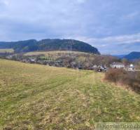 Stavebný pozemok s krásnym výhľadom nad obcou Jasenica pri Považskej B - Krajina v Záhradách Jasenice: Zeleň, kopce a domčeky pod oblačným nebom.