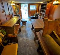 PRIPRAVUJEME Rekreačná chata - Zvolen - Kováčová na Predaj - Interiér chaty s drevenými stolmi a lavicami, výhľad na záhradu.