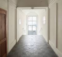 Exkluzívne | Na predaj výnimočný 2i byt pri Trnavskom mýte  - Chodba s dlaždicami a bielymi stenami vedie k presklenej bráne na ulici Vajnorská.