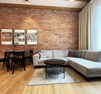 Exkluzívne | Na predaj výnimočný 2i byt pri Trnavskom mýte  - Obývačka s tehlovou stenou, sedačkou, stolom a obrazmi; svetlý priestor na ulici Vajnorská, Bratislava.