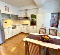 Na predaj – svetlý 2-izbový byt s loggiou a garážou | Bratislava - Kuchyňa v 2-izbovom byte s podlahou s dreveným dekorom, bielou linkou a nerezovou chladničkou.