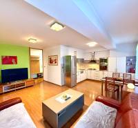 Na predaj – svetlý 2-izbový byt s loggiou a garážou | Bratislava - Interiér 2-izbového bytu s podlahou s dreveným dekorom, kuchyňou a obývačkou.