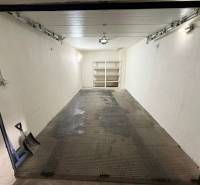 Na predaj – svetlý 2-izbový byt s loggiou a garážou | Bratislava - Priestranná garáž s poličkami, oceľovou podlahou a lopatou v rohu.