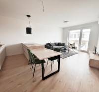Na prenájom kompletne zariadený 2i byt s parkingom, Nový Ružinov - Svetlá obývacia izba v 2-izbovom byte s podlahou s dreveným dekorom, pohodlným gaučom a jedálenským stolom.