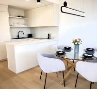 Prenájom 3-izbový byt s loggiou, SKY PARK, Bratislava - Kuchynský kút s bielymi skrinkami, skleneným stolom a podlahou s dreveným dekorom v 3-izbovom byte.