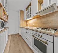 Ponúkame na predaj 3-izb.byt Vígľašská ul., Bratislava - Petržalka. - Kuchyňa v 3-izbovom byte s podlahou s dreveným dekorom, bielymi skrinkami a spotrebičmi.