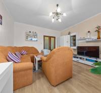 Ponúkame na predaj 3-izb.byt Vígľašská ul., Bratislava - Petržalka. - Obývacia izba v 3-izbovom byte s oranžovým gaučom a podlahou s dreveným dekorom.