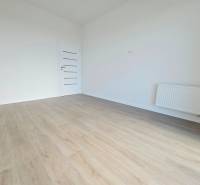 3i. BYT S VLASTNÝM TEP. ČERPADLOM + KLIMATIZÁCIA A EXTERIÉROVÉ ŽALÚZIE - Izba v 3-izbovom byte s drevenou podlahou a bielymi stenami.