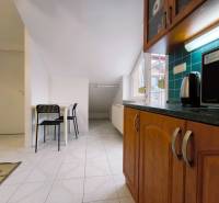 | 2i byt v rodinnom dome | 65 m | Bratislavská | Záhorská B. - Kuchyňa v rodinnom dome s drevenými skrinkami, stolom a dvoma čiernymi stoličkami.