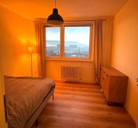 Prenájom pekný 3 izbový byt Jankolova ulica, Bratislava V. Petržalka - Spálňa so stolíkom v 3-izbovom byte, s podlahou s dreveným dekorom a výhľadom z okna.