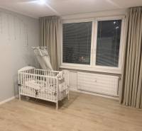  Prenájom 3-izbový byt, Nové Zámky - Detská postieľka v 3-izbovom byte s podlahou s dreveným dekorom a sivými závesmi.