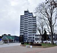 Kancelária s výhľadom na centrum Michaloviec. 16 m2 - Kancelárie na Námestí slobody v Michalovciach, vysoká budova s oknami a stromami v okolí.