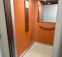 2-izbový byt novostavba s podzemným parkovaním- bez rezervačnej zálohy - Oranžový interiér moderného výťahu so zrkadlom a kovovým madlom.