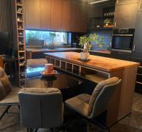 2-izbový byt v Pezinku s vlastným parkovaním - REZERVOVANÉ - Kuchyňa v 2-izbovom byte s čiernymi skrinkami a podlahou s dreveným dekorom.