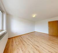 Na prenájom 2 izbový byt, Dežerice - Izba s podlahou s dreveným dekorom v 2-izbovom byte a veľkým oknom.