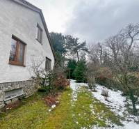 Predaj rekreačná chata s pozemkom, garážou a saunou Modra, Harmónia - Záhrada pri chate v Modre s trávnikom, snehom a drevinami pozdĺž domu.