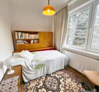 Predaj rekreačná chata s pozemkom, garážou a saunou Modra, Harmónia - Izba v chate s poličkou na knihy, posteľou a veľkým oknom.