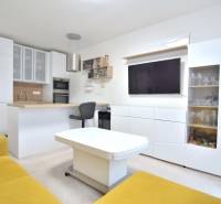 ŠTÚROVA, 3-i byt, 75 m2 – komplet rekonštrukcia, vlastné parkovanie - Obývacia izba s kuchyňou v 3-izbovom byte, biela nábytok, žltá sedačka, televízor.