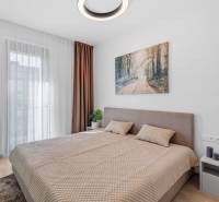 I Prenájom exkluzívneho 2-i bytu v projekte Metropolis - Spálňa s veľkou posteľou, závesmi a podlahou s dreveným dekorom v 2-izbovom byte.