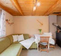 Záhradná chatka Handlová - Interiér chaty s kachľovou pecou, zelenou sedačkou a stolom. Drevený strop a dekorácie.