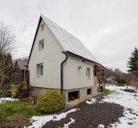 Záhradná chatka Handlová - Chata v Handlovej s trávnikom a zasneženou záhradou, obklopená stromami a kríkmi.