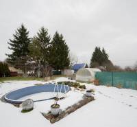Záhradná chatka Handlová - Zasnežená záhrada pri chate v Handlovej s bazénom, skleníkmi a ihličnatými stromami.