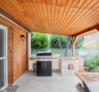 Záhradná chatka Handlová - Drevené obloženie a gril na terase chaty v Handlovej, vedľa zelených kríkov.