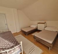 Viacgeneračný rodinný dom / investičná nehnuteľnosť – Dolná časť Zobor - Spálňa v rodinnom dome s tromi posteľami a podlahou s dreveným dekorom.