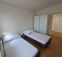 Viacgeneračný rodinný dom / investičná nehnuteľnosť – Dolná časť Zobor - Izba v rodinnom dome s dvomi posteľami, skriňou a podlahou s dreveným dekorom.