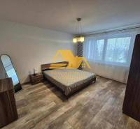 Prenajmem 3 izbový byt s loggiou v Nových Zámkoch - Spálňa v 3-izbovom byte s posteľou, zrkadlom a podlahou s dreveným dekorom.