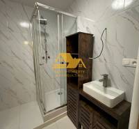 Prenajmem prerobený 2 izbový byt s balkónom v Nových Zámkoch - Kúpeľňa v 2-izbovom byte s bielymi dlaždicami, sprchovacím kútom a umývadlom na skrinke.