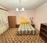 Predám rodinný dom s garážou v obci Dvory nad Žitavou - Spálňa v rodinnom dome s kobercom a nábytkom, jemné ružové tapety.