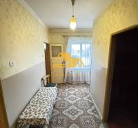 Predám rodinný dom s garážou v obci Dvory nad Žitavou - Chodba v rodinnom dome s kobercovým dekorom a stolom, okno na konci miestnosti.