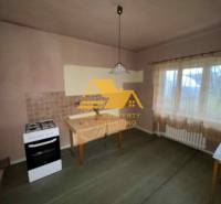 Predám rodinný dom s garážou v obci Dvory nad Žitavou - Kuchyňa v rodinnom dome so sporákom, stolom, záclonou a svetlom dekorom stien.