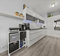 KOMPLETNE ZARIADENÝ 2-IZB. BYT,BALKÓN + PIVNICA,BUDATÍNSKA – PETRŽALKA - Kuchyňa v 2-izbovom byte s bielymi skrinkami a podlahou s dreveným dekorom.