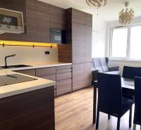 PRENÁJOM NÁDHERNÝ 3-IZBOVÝ BYT MAMAPAPA BA IV DÚBRAVKA - Kuchyňa v 3-izbovom byte s tmavým nábytkom a podlahou s dreveným dekorom.