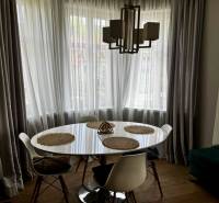 Prenájom veľkého luxusného 2izb bytu pri Bratislavskom hrade - Jedálenský kút v 2-izbovom byte s okrúhlym stolom, závesmi a podlahou s dreveným dekorom.